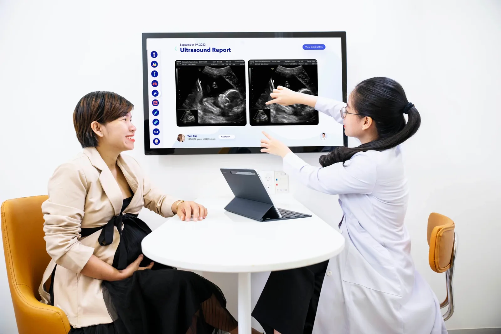 A doctor showing an ultrasound report to a patient on a wall display